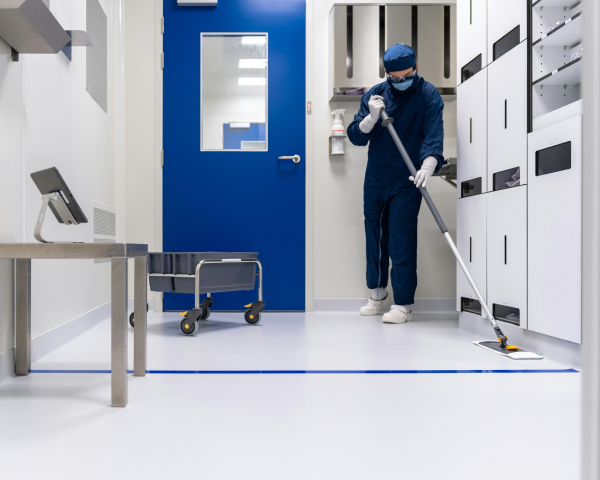 Cleaner in blue gloves wiping an office desk with a spray bottle and cloth